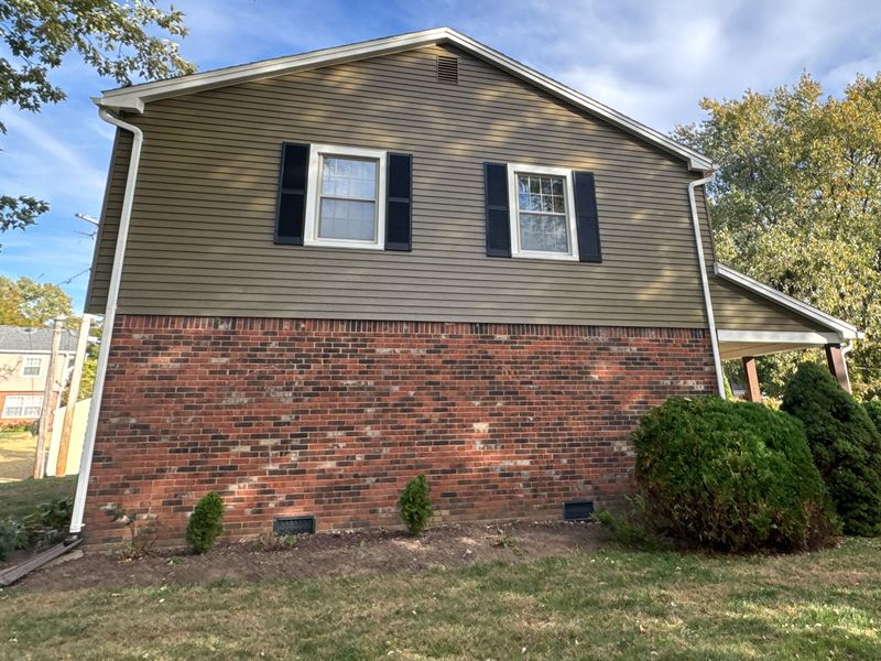 The same gable end after two coats: olive siding, black shutters, white trim and a white downspout
